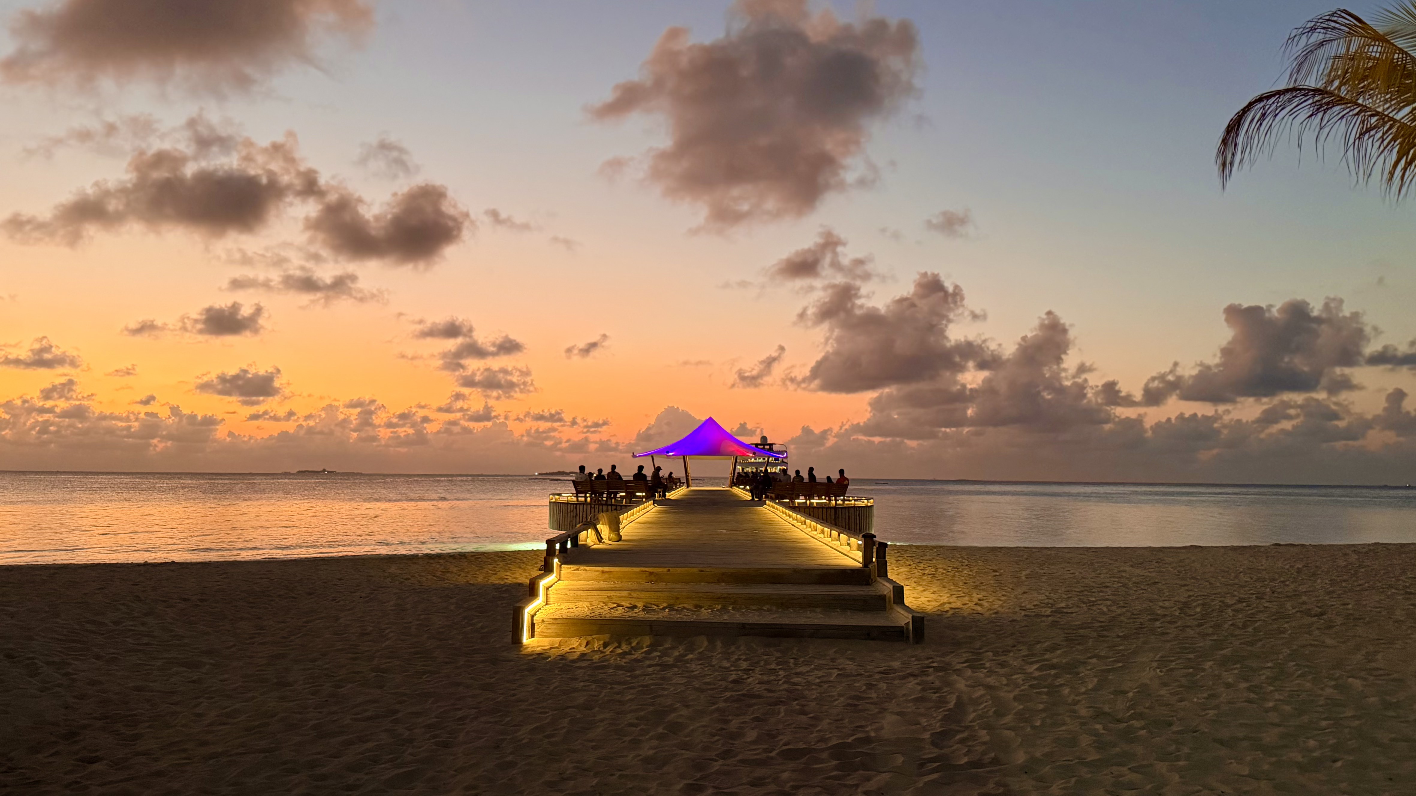 A beachside jetty glowing at sunset on Dhangethi Island